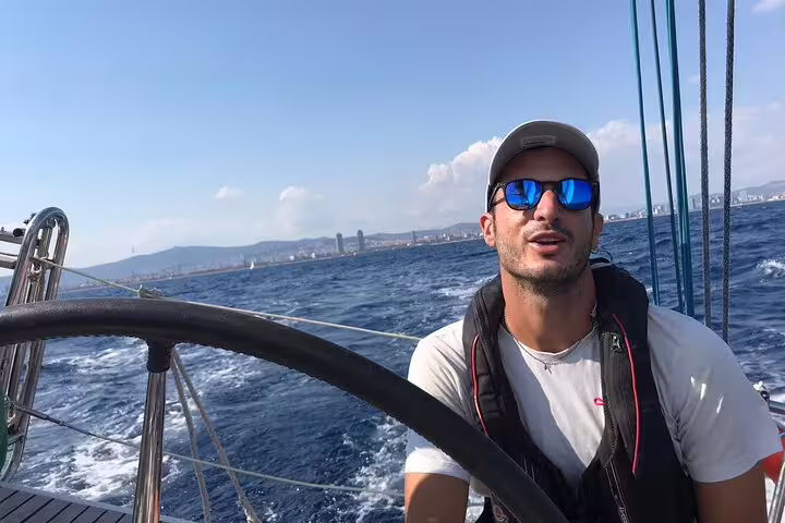 Man steering sailboat on a sunny day during a 2-hour sunset sailing experience with open bar and tapas, picturesque ocean view.