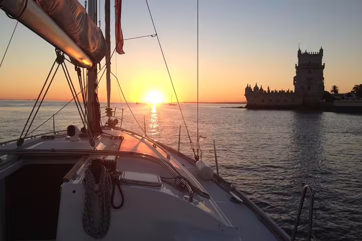 View from a sailboat approaching Belém Tower during a vibrant sunset on the Tagus River in Lisbon.