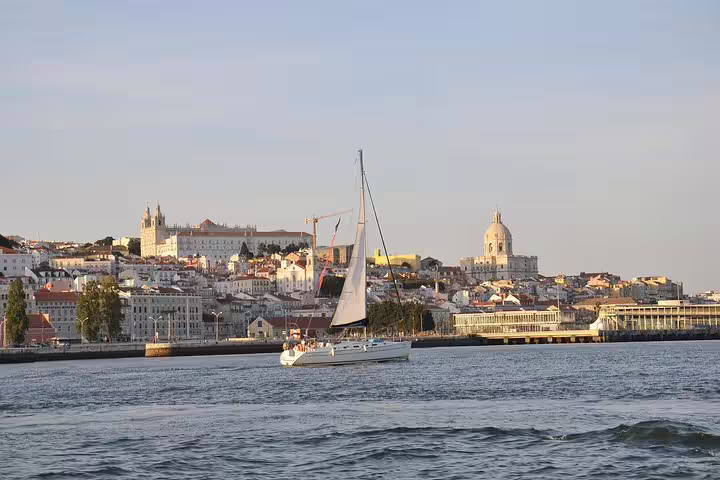 Sailboat cruising on the Tagus River with Lisbon's iconic bridge in the background under a clear blue sky.