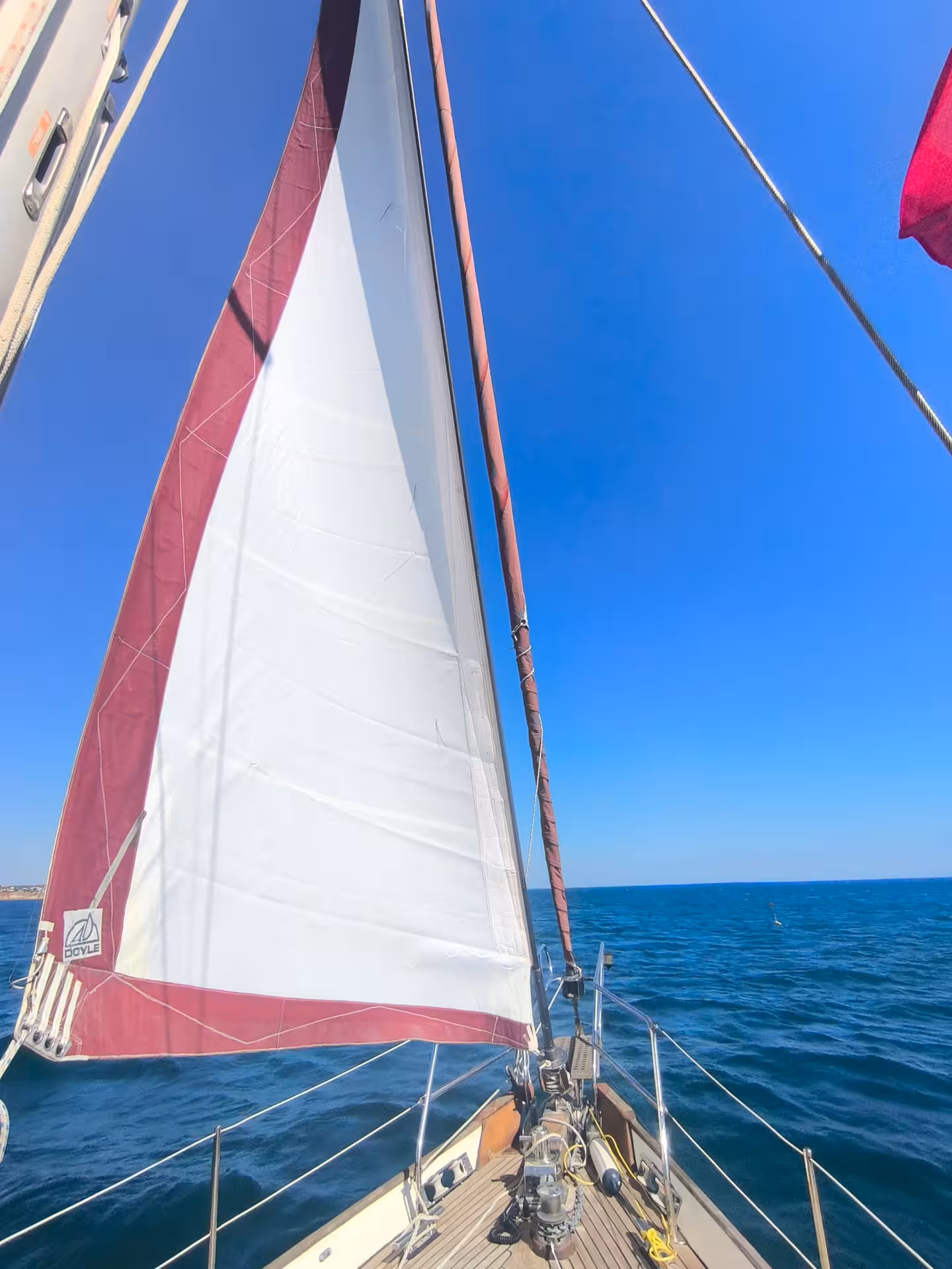 White and burgundy sail unfurled on a classic sailboat gliding across the blue sea in Portimao Algarve