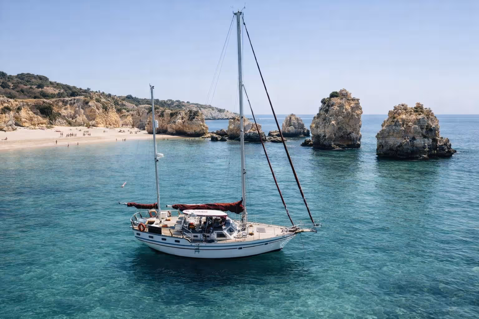 Elegant sailboat anchored in turquoise waters near Portimao's stunning rocky coastline on a romantic sunset sailing tour