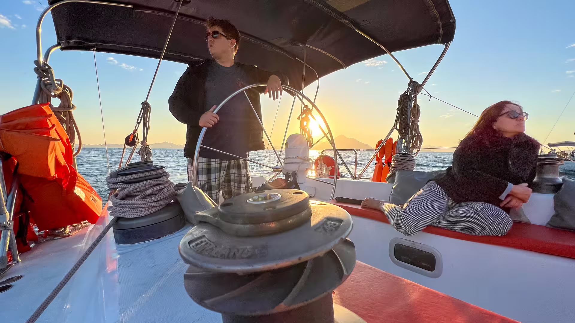 Sunset whale watching expedition on a sailboat with guests relaxing on deck and skipper at helm