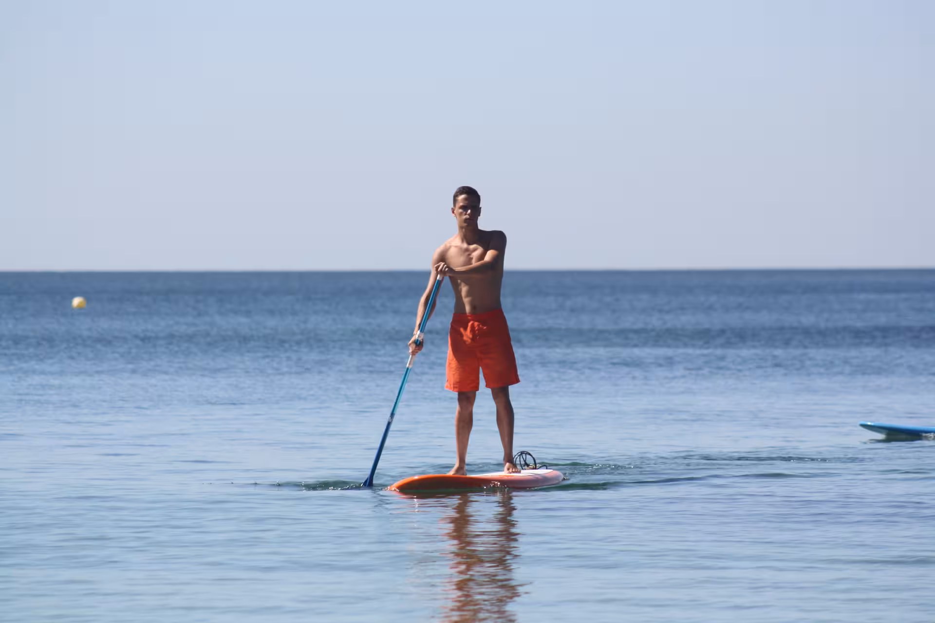 Young man in red shorts standing confidently on a SUP board rental paddling on serene ocean water