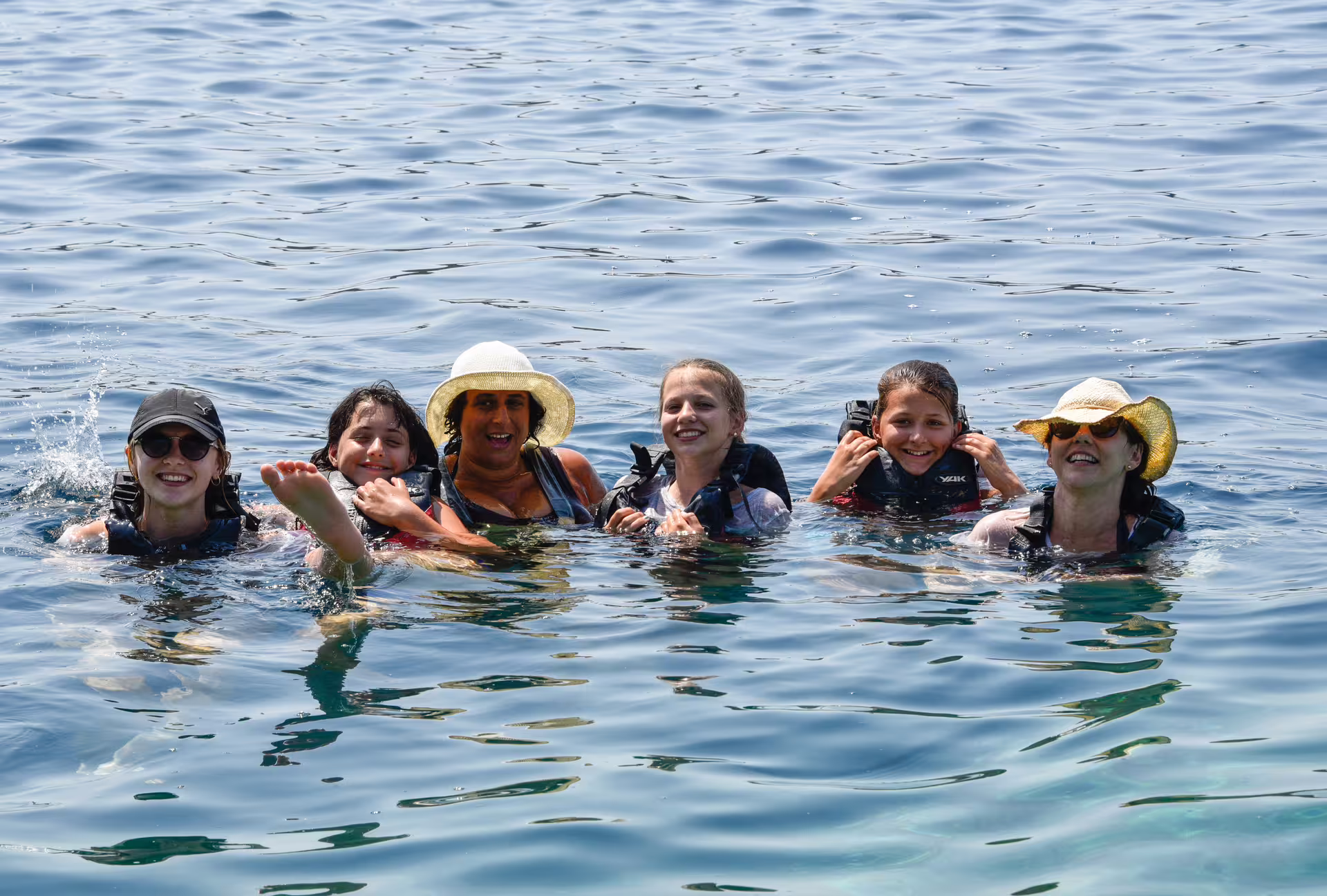 Smiling group floating in the sea on a SUP in Kardamyli break, Mani coast, with life vests and sun hats