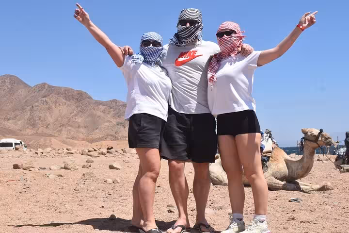 Friends posing in Sinai desert on Super Colored Canyon jeep adventure from Sharm El Sheikh, with camel and Blue Hole