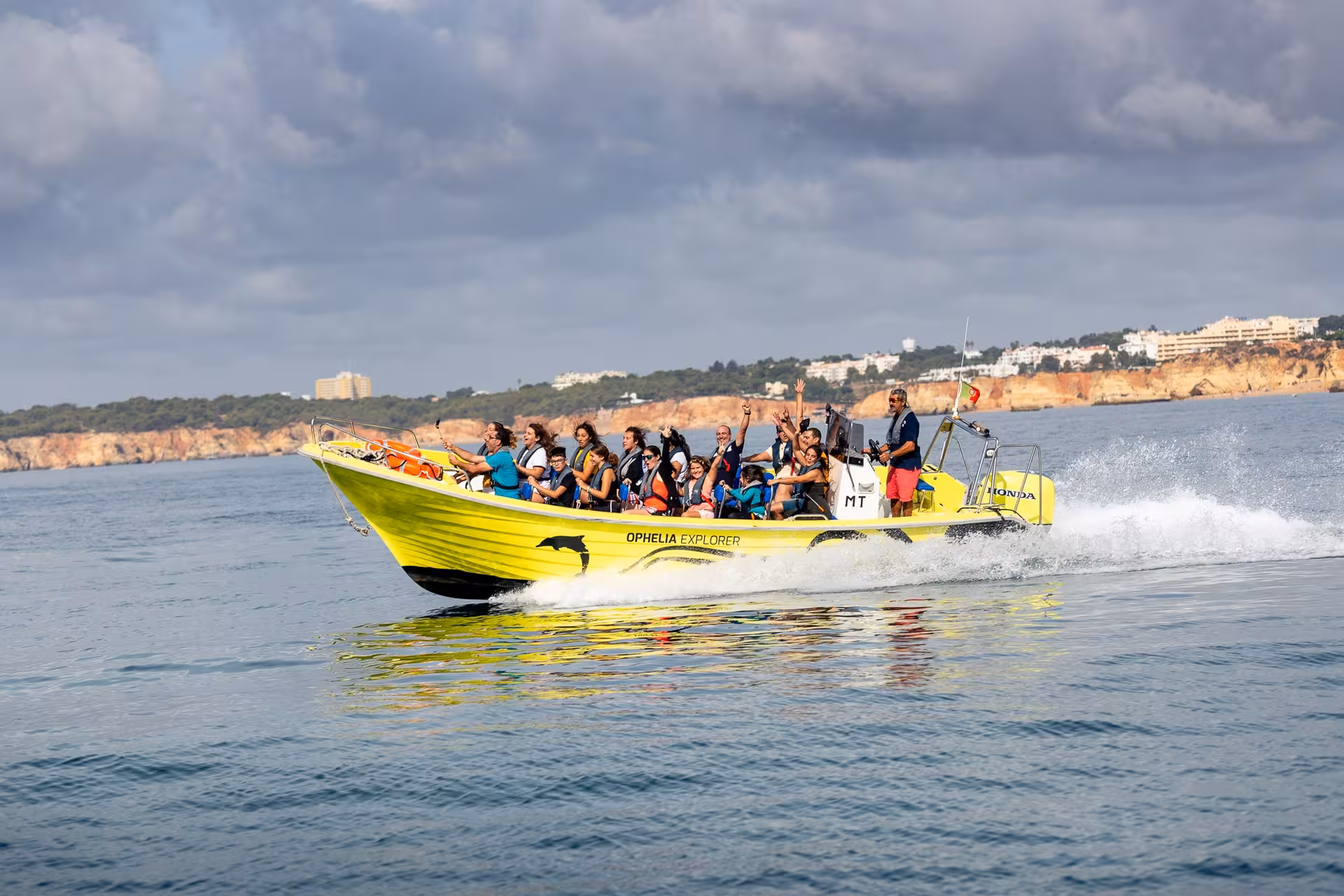 Excited passengers on the Super Dia yellow speedboat racing along the Algarve coastline on a thrilling ocean adventure tour
