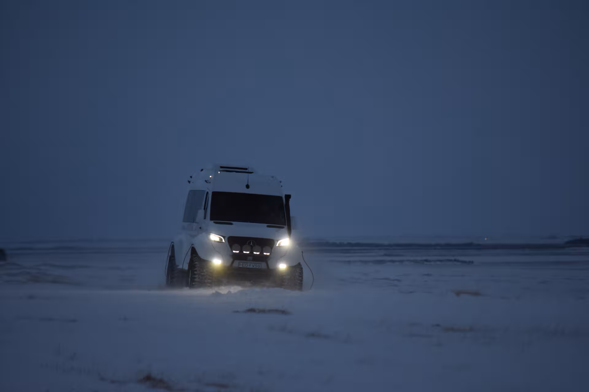 White Mercedes super jeep driving across snowy Iceland landscape at dusk with headlights on