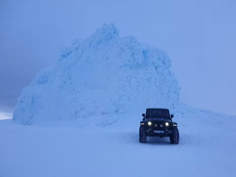 Black Super Jeep with headlights on parked in front of a massive ice formation on Eyjafjallajokull Glacier, Iceland
