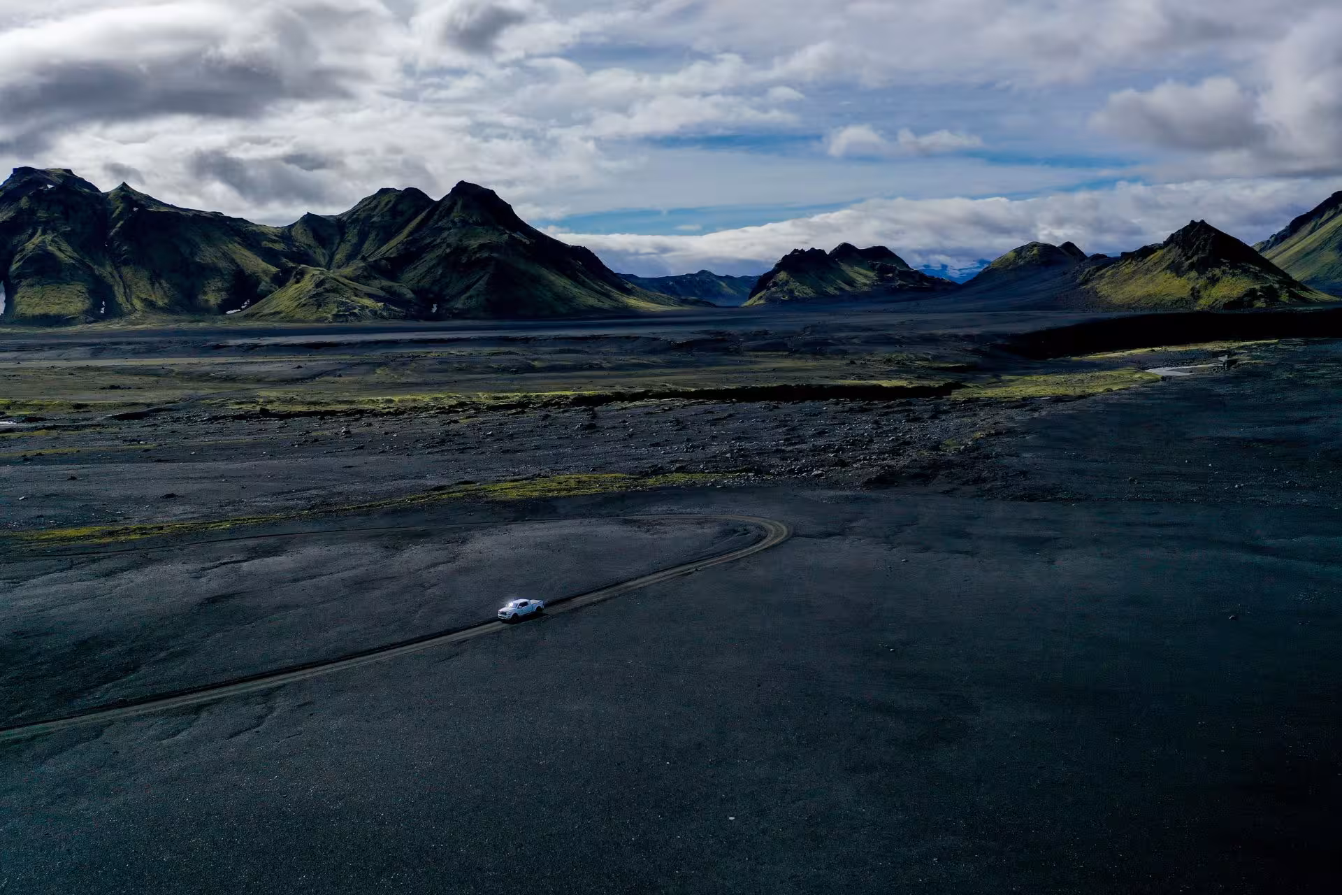 White super jeep driving on black volcanic terrain with green moss-covered mountains in Fjallabak Nature Reserve, Iceland