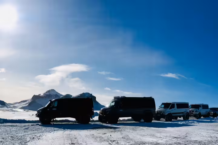 Fleet of super jeeps parked on snowy glacier landscape with mountain backdrop and blue sky