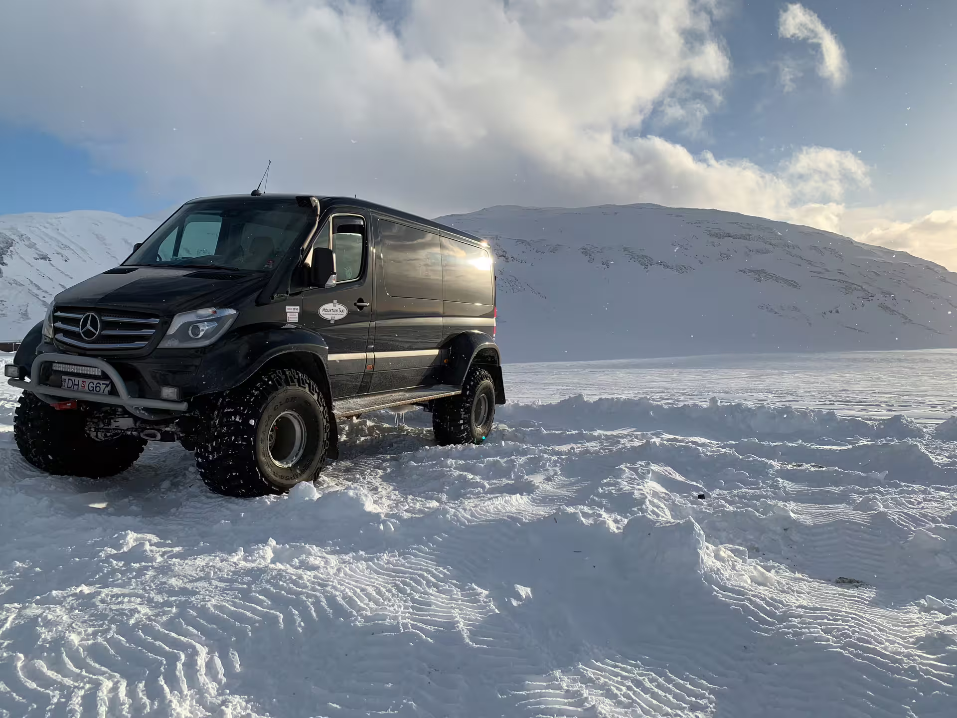 Black Mercedes Sprinter super jeep on snowy glacier landscape with snow-covered mountains in Iceland