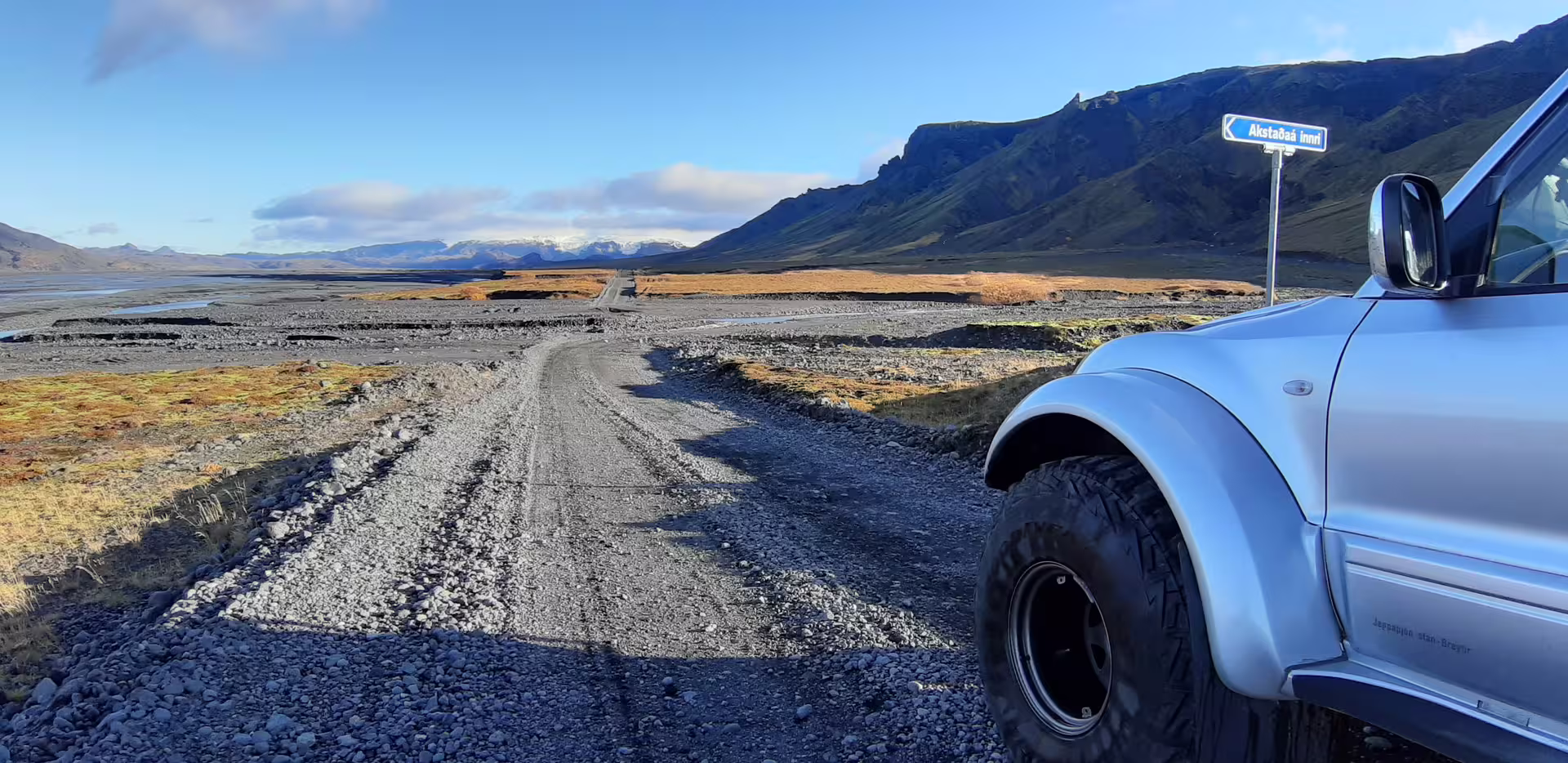 Silver super jeep on gravel road in Iceland with dramatic black mountains and golden plains toward Thorsmork