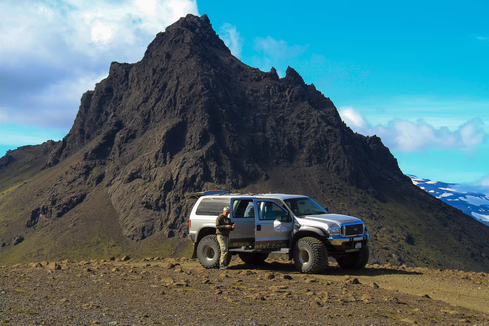 Super jeep 4x4 parked on volcanic highland terrain with dramatic dark mountain peak in Iceland
