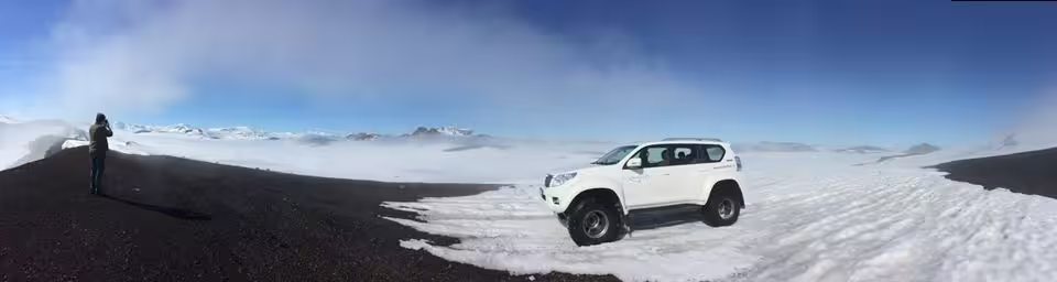 White super jeep on snowy Icelandic highland plateau with panoramic mountain views under blue sky