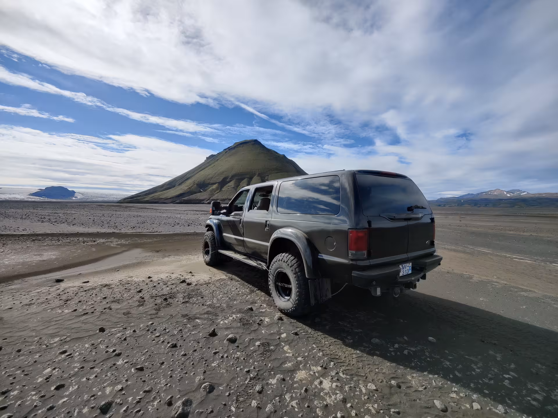 Modified super jeep on volcanic black sand plain with Mælifell volcano in Iceland's Fjallabak highlands