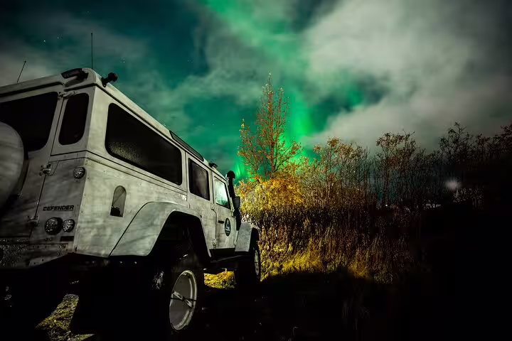 White Land Rover Defender super jeep parked under vibrant green northern lights in Iceland