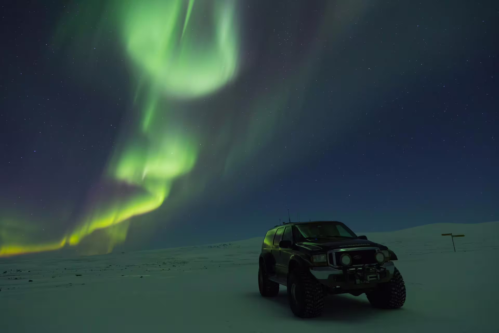 Super jeep parked on snowy Iceland landscape under vivid green northern lights aurora borealis at night