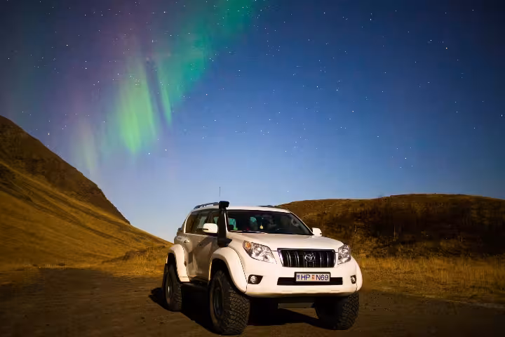 White Toyota Land Cruiser super jeep parked under vibrant green northern lights in Iceland