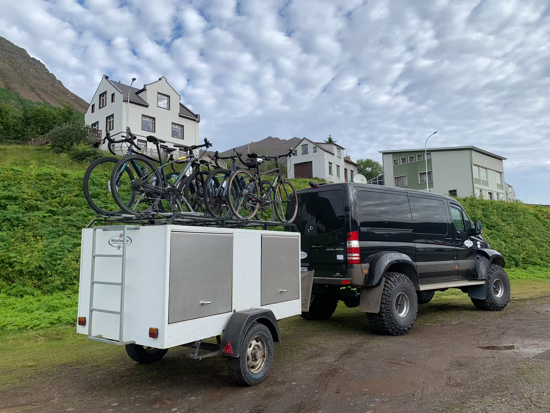 Black Mercedes Super Jeep towing white trailer loaded with bicycles on roof in Iceland