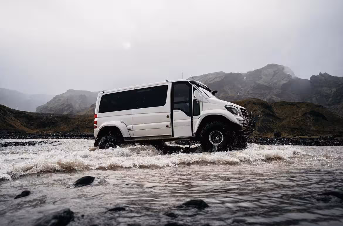 White 4x4 super jeep crossing a glacial river in Iceland with misty mountains in background