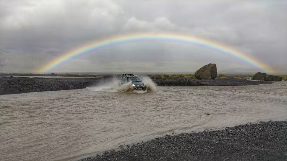 Super jeep crossing flooded river with full rainbow over Thorsmork highlands Iceland