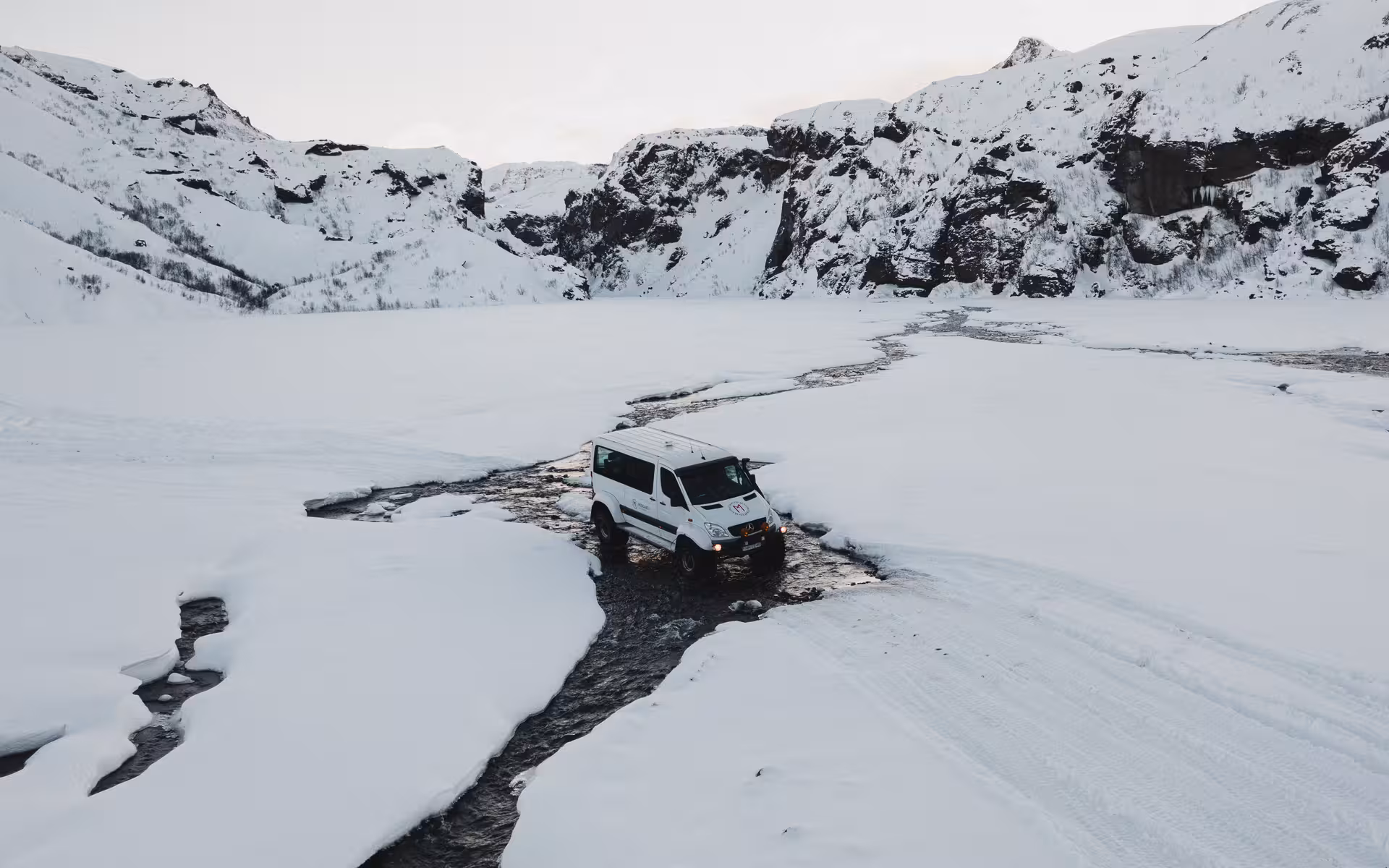 White Super Jeep van crossing a snowy river stream in Thorsmork valley, Iceland, surrounded by snow-covered mountains