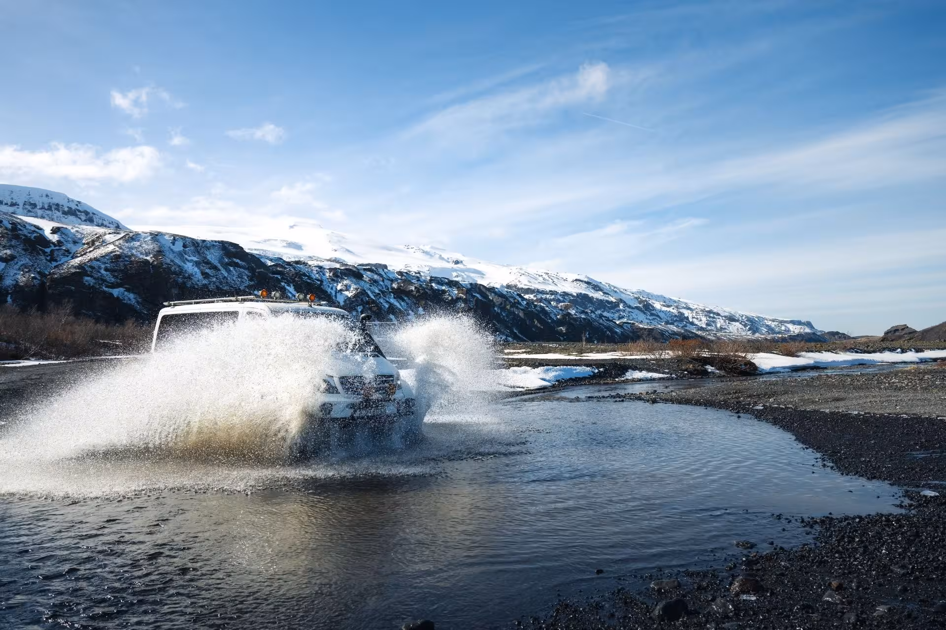 White super jeep crossing a glacial river with snow-capped mountains in Thorsmork, Iceland