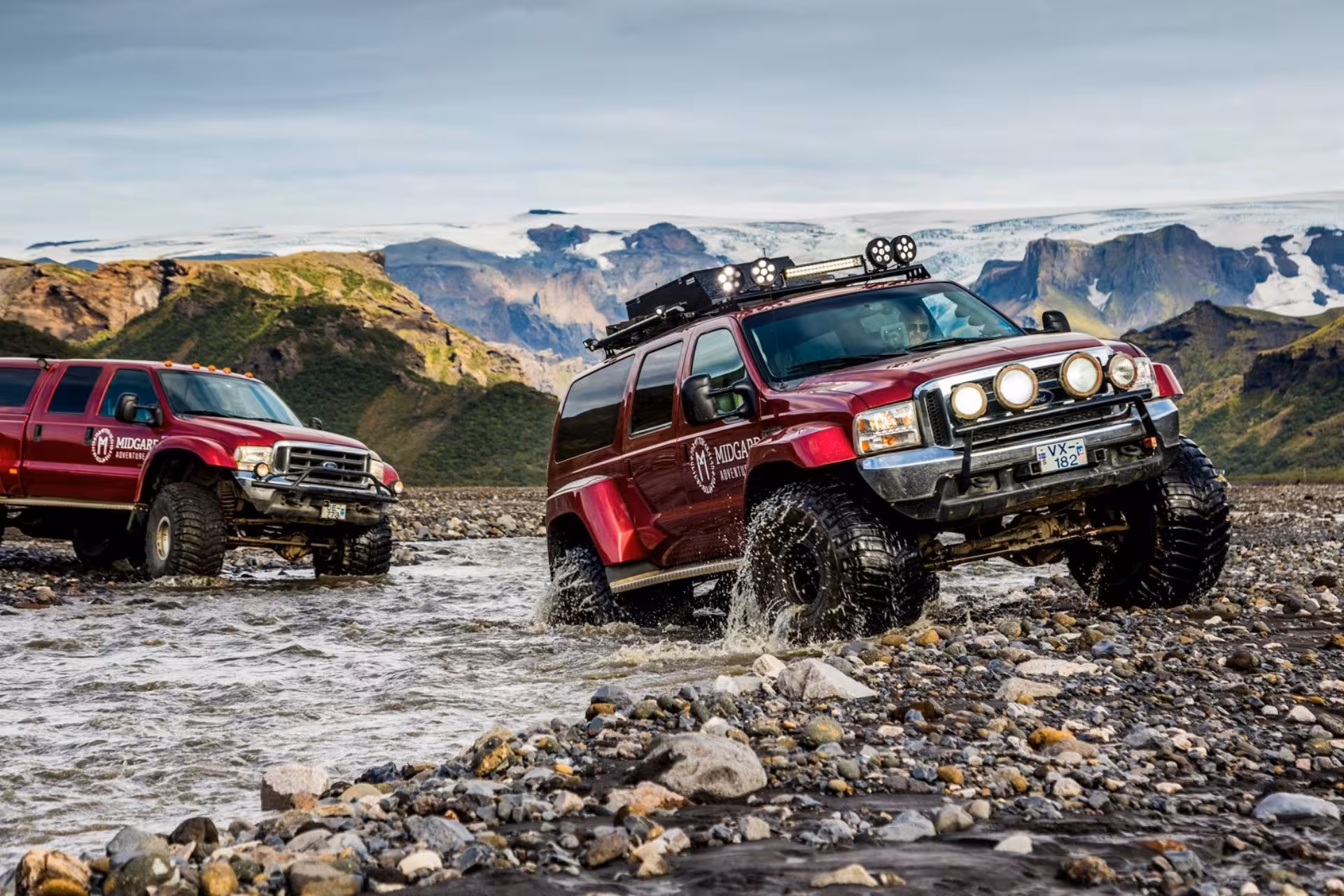 Two red Midgard Adventures super jeeps crossing a rocky glacial river in Thorsmork Iceland