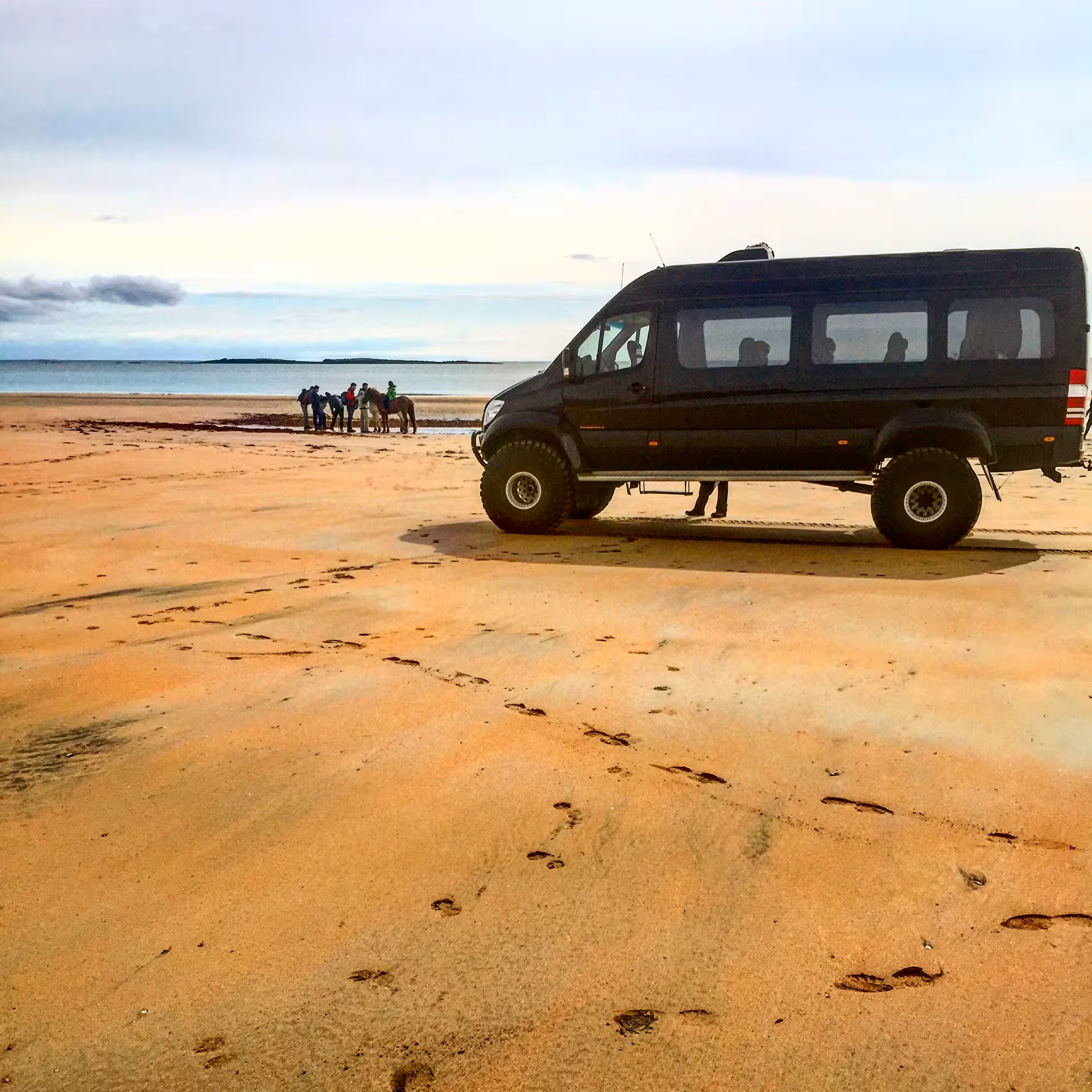 Black super jeep 4x4 van on sandy beach with group and horses near Snaefellsnes Peninsula, Iceland