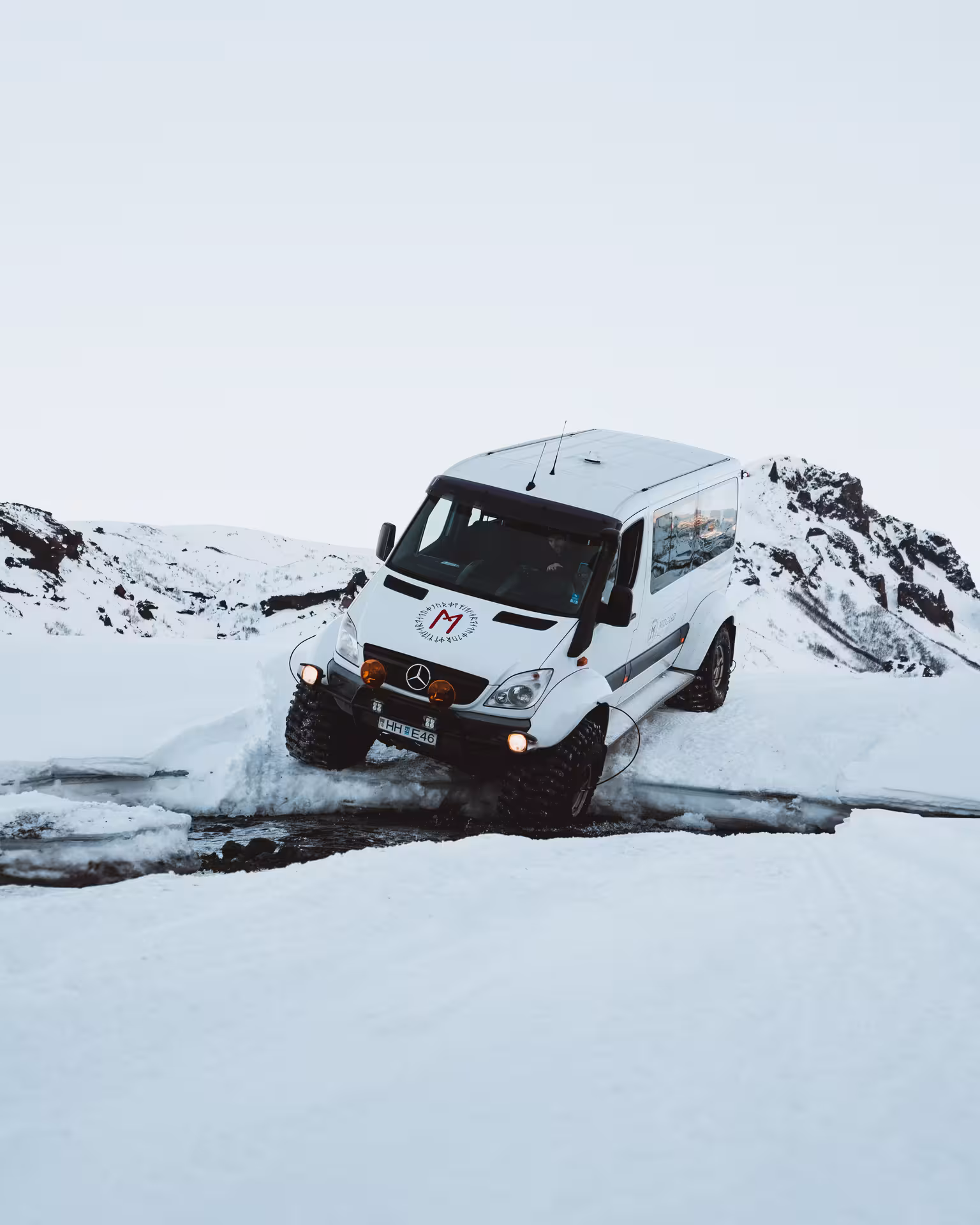 White Mercedes Sprinter super jeep crossing icy stream in snowy Thorsmork mountains Iceland