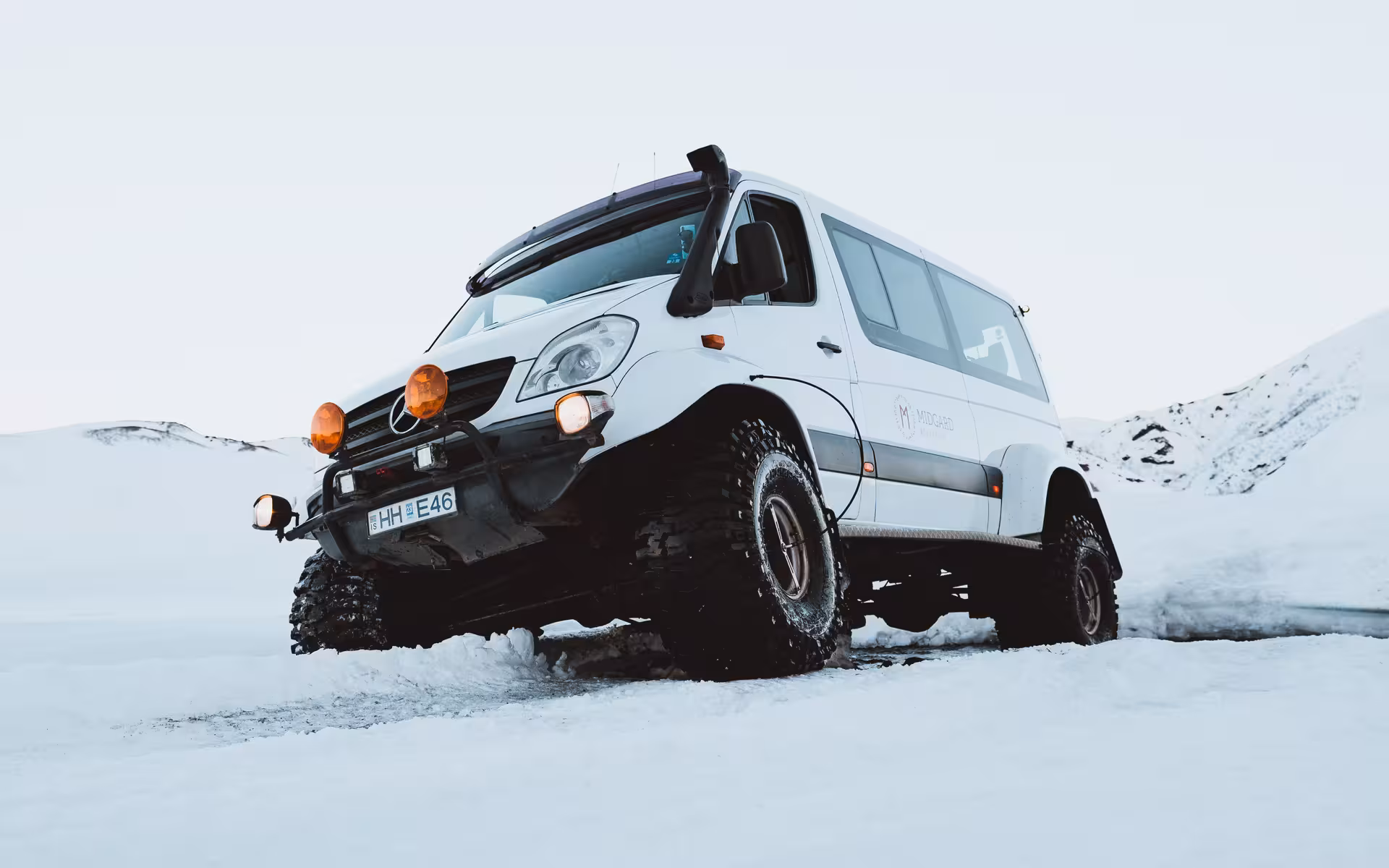 White Mercedes Sprinter super jeep with oversized tires driving through snowy Icelandic landscape