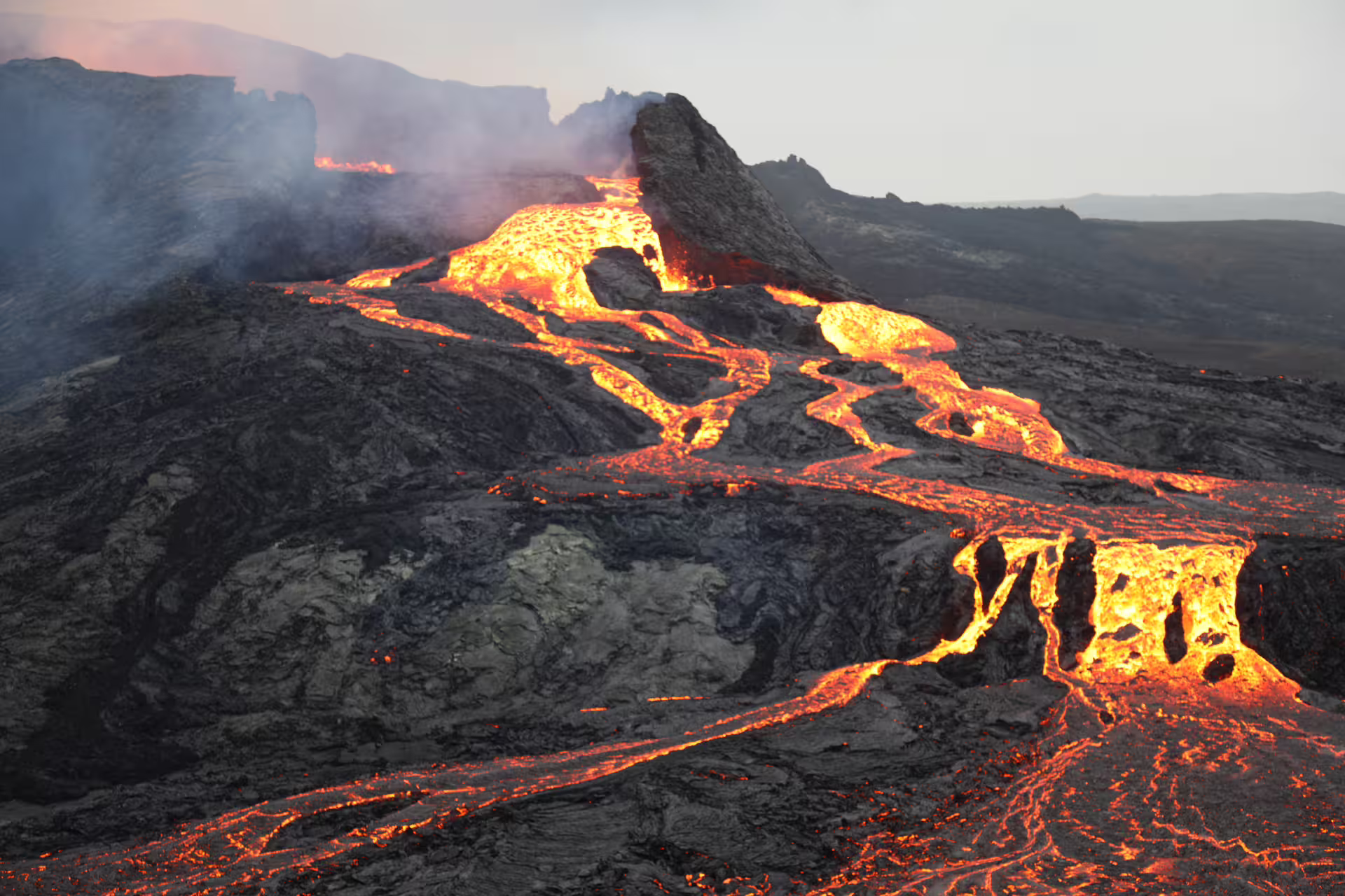 Glowing lava flows streaming down a volcanic landscape during an active eruption with smoke rising