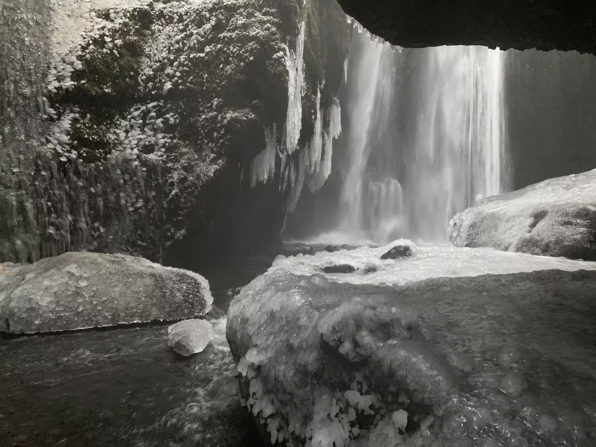View from behind a frozen waterfall with icicles and snow-covered rocks in winter Iceland
