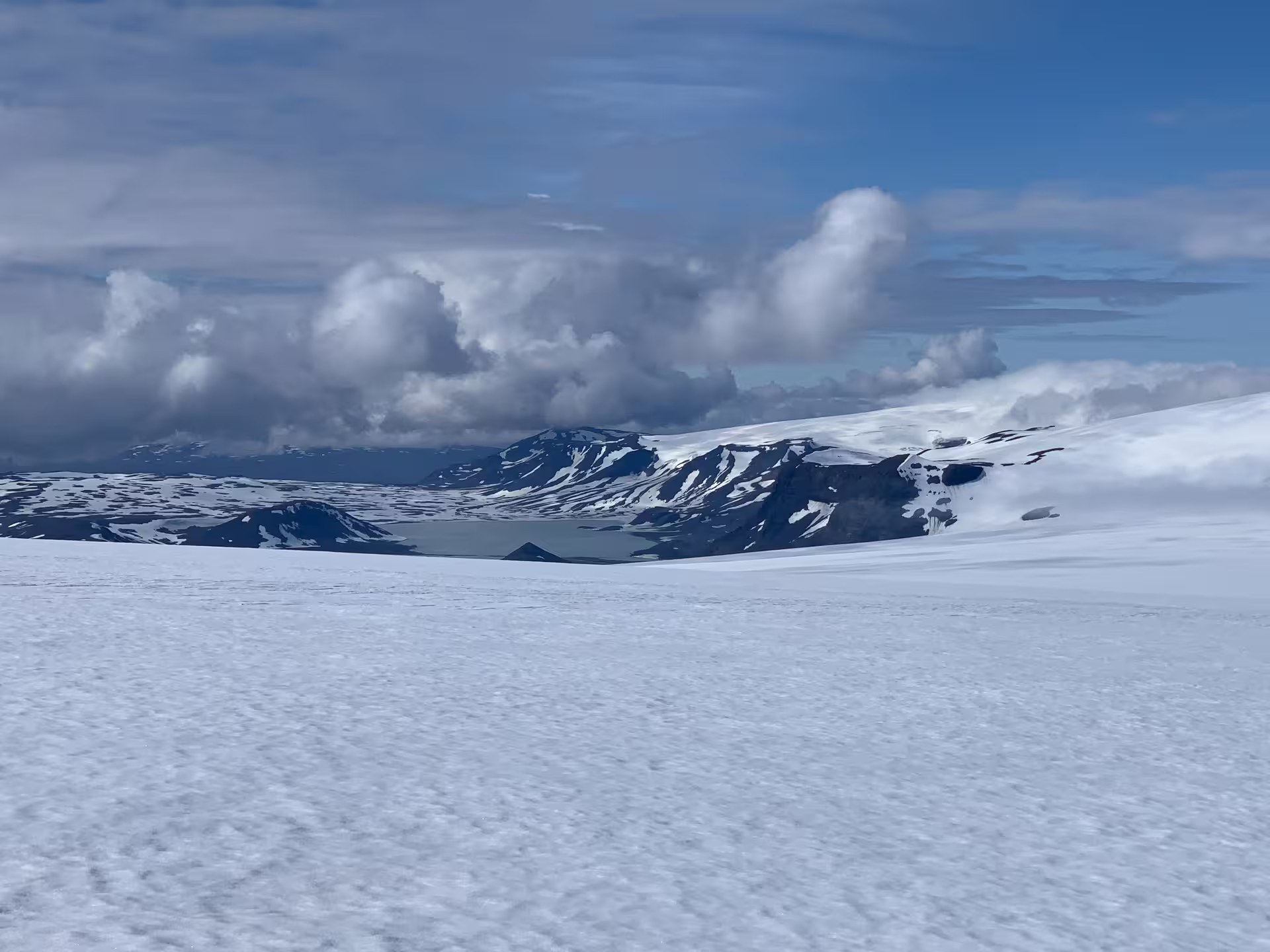 Vast snow-covered glacier plateau with volcanic mountains and a glacial lake under a blue sky in Iceland