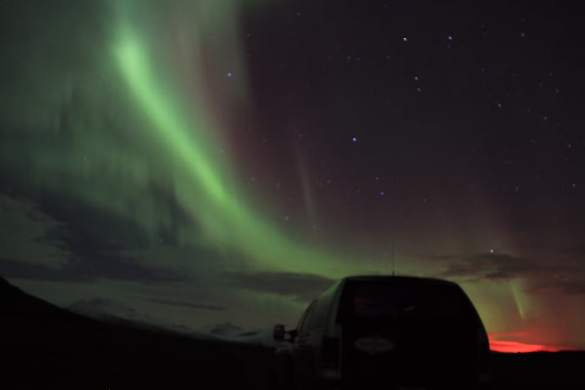 Northern lights aurora borealis arching over a super jeep on a dark Icelandic night
