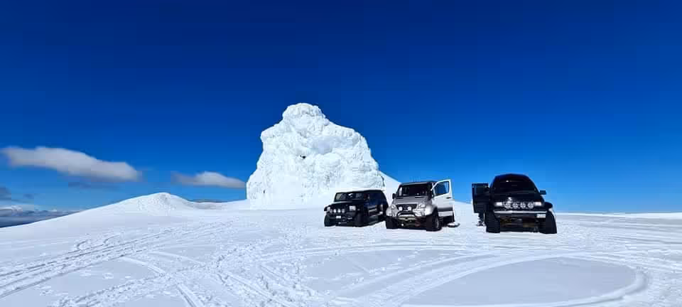 Three super jeeps parked on Eyjafjallajokull glacier beside a large ice formation under a clear blue sky