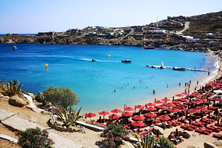 Super Paradise Beach Mykonos with turquoise bay, boats and red sunbeds on island sights and beaches tour