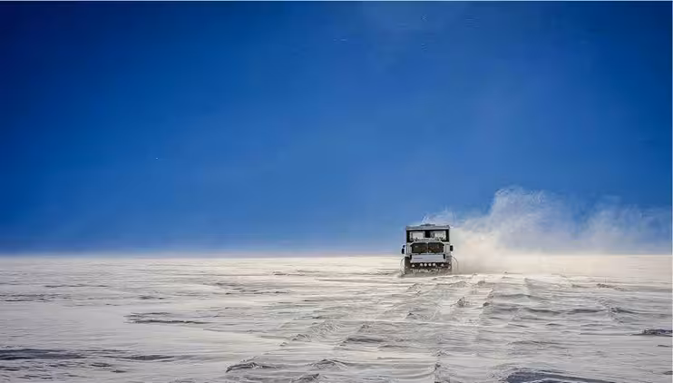Superjeep driving across vast snowy glacier landscape in West Iceland under clear blue sky