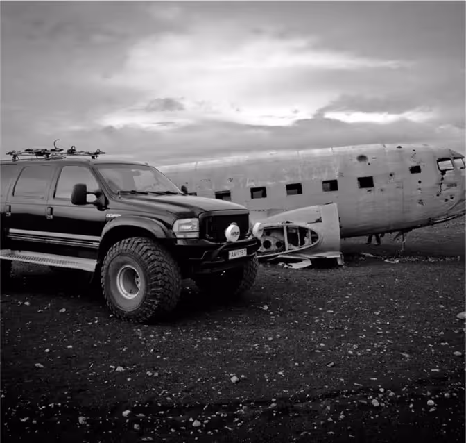 A powerful superjeep parked beside the iconic DC-3 plane wreck on Iceland's black sand beach during a South Coast tour.