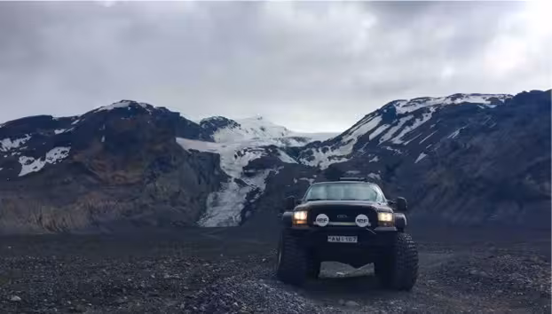 Black superjeep with headlights on parked on rocky terrain before snowy Eyjafjallajokull glacier mountains