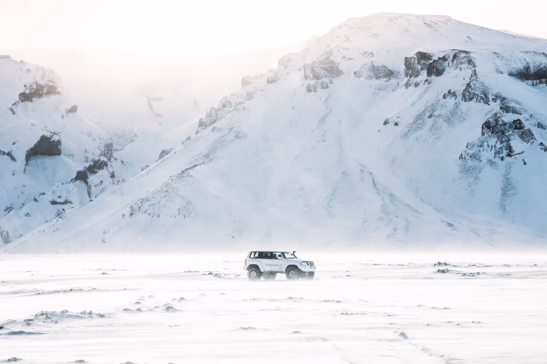 White superjeep crossing snowy Thorsmork Valley with dramatic snow-covered mountains in Iceland