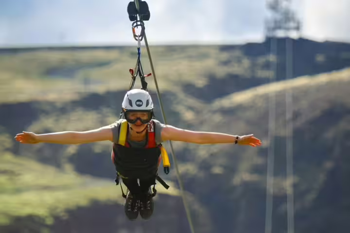 Thrill-seeker enjoys Superman Ride zipline adventure, soaring above scenic landscapes with arms outstretched like a falcon.