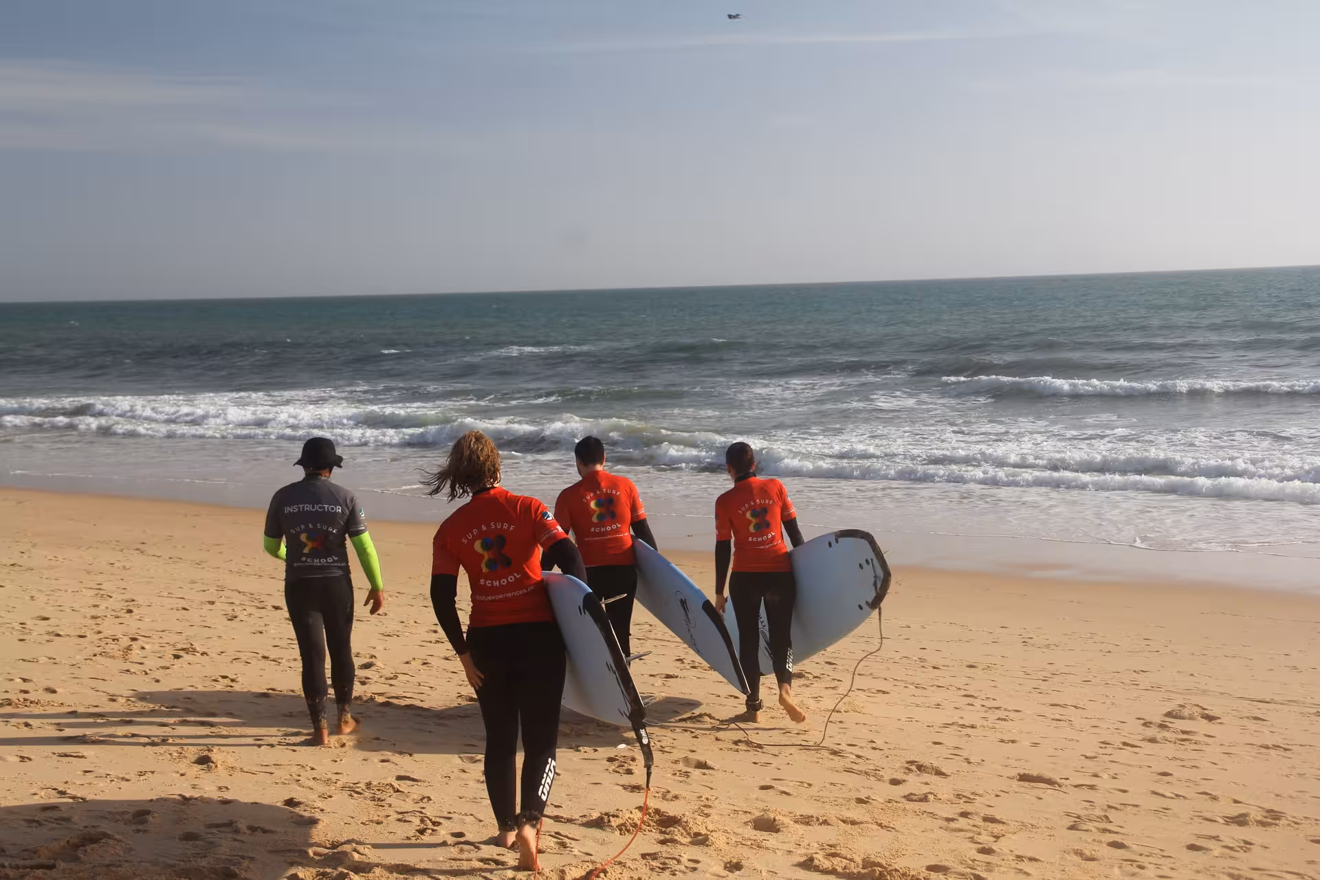 Surf instructor leading a small group carrying foam boards to the shoreline for a guided surf experience