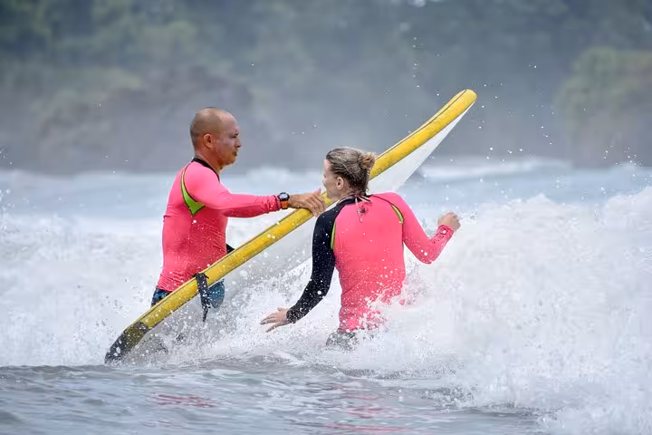 Surf instructor guiding student through waves with a yellow board in Manuel Antonio, highlighting expert Costa Rica surf lessons.