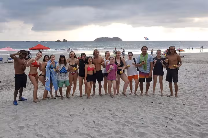 Group of people enjoying a day on Manuel Antonio Beach with island backdrop, perfect for surf lessons and relaxation.
