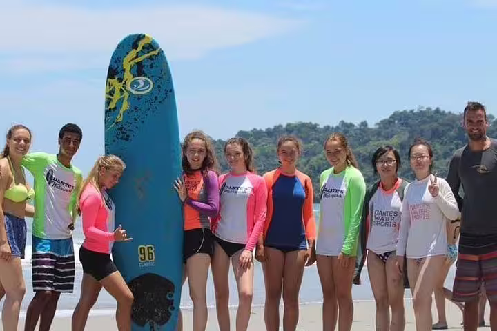 Group of young surfers in Manuel Antonio pose with their surfboard, enjoying a sunny day of learning and fun.
