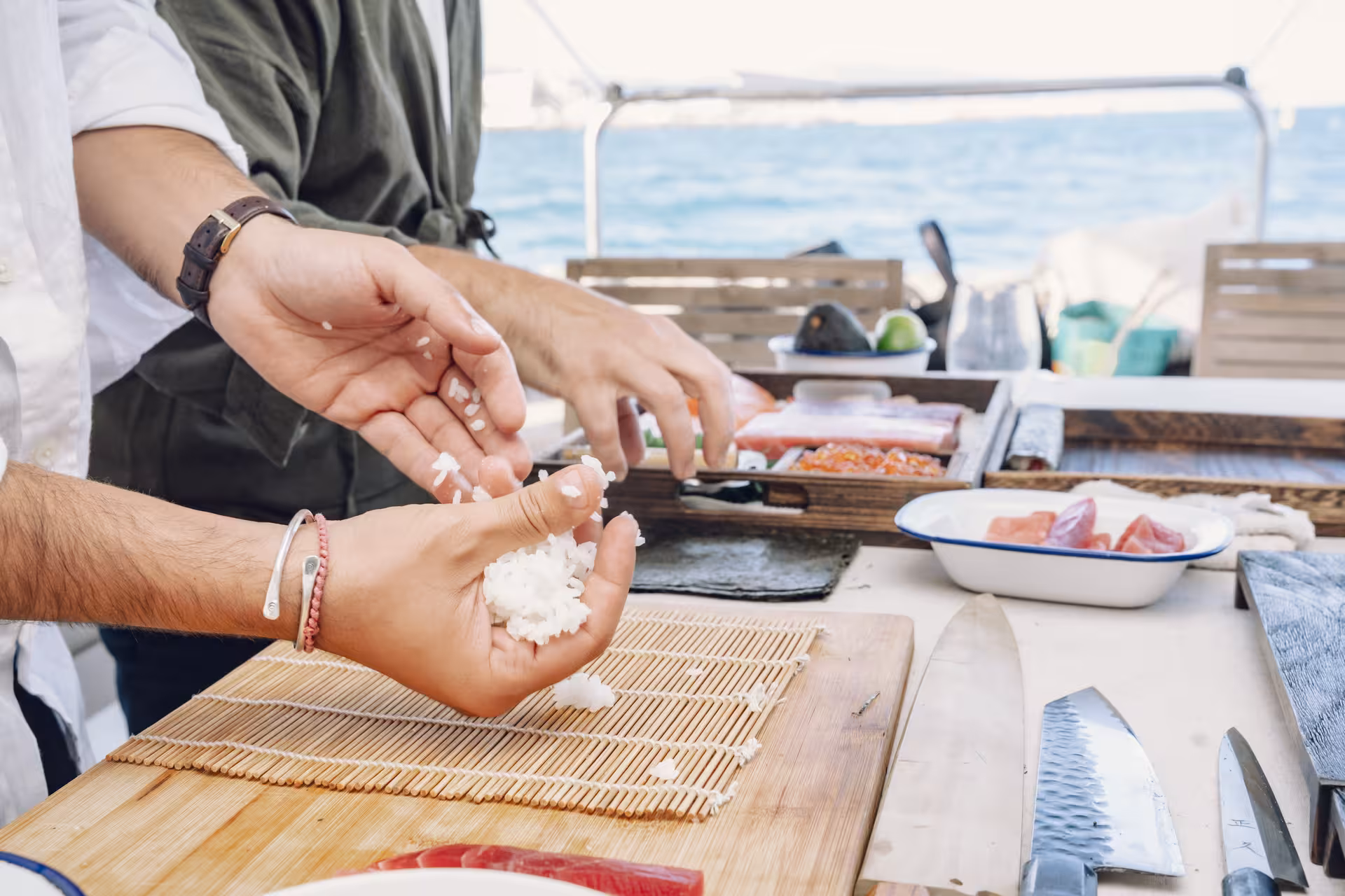 Hands shaping sushi rice on a bamboo mat with fresh fish and knives during a sushi masterclass workshop