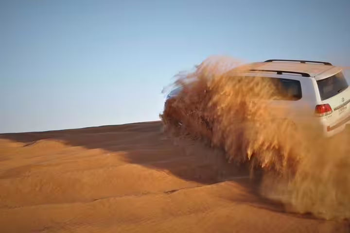 Powerful SUV kicking up sand as it speeds over massive desert dunes during a safari adventure.
