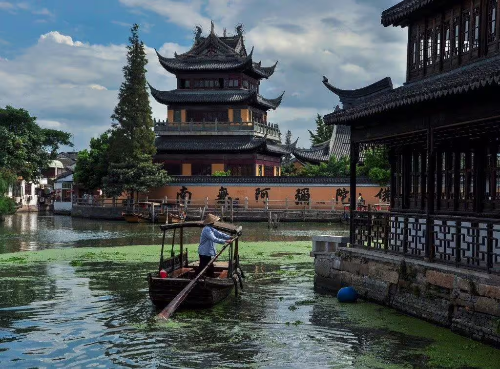 Boatman navigating tranquil canal waters in Suzhou, with iconic Chinese temples and scenic views in the background.