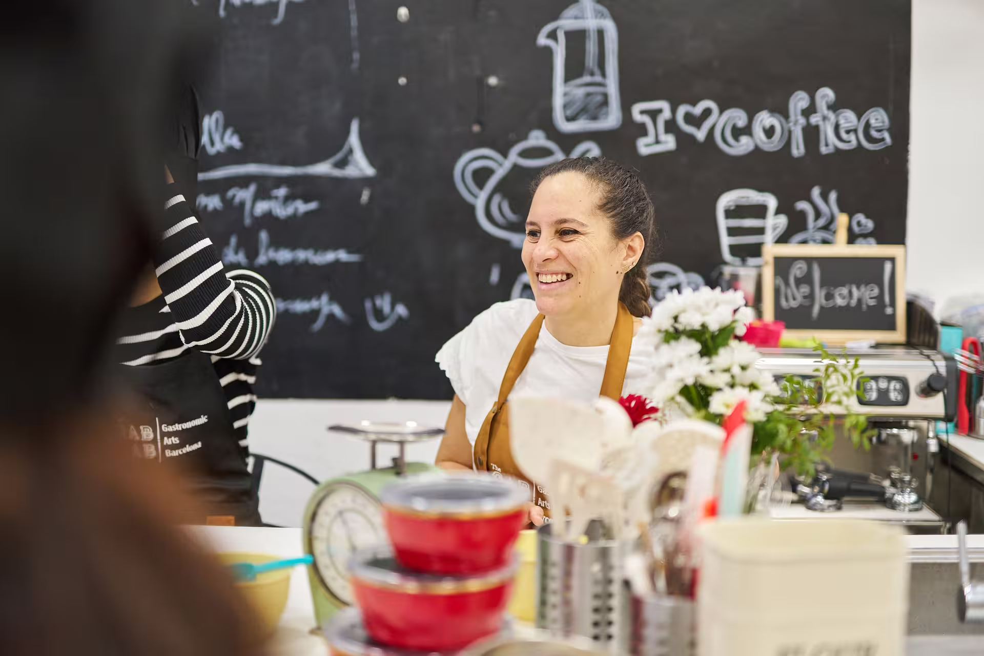 Smiling instructor in a cozy kitchen during the Sweet Escape Bake & Take Workshop, surrounded by baking tools and decor.